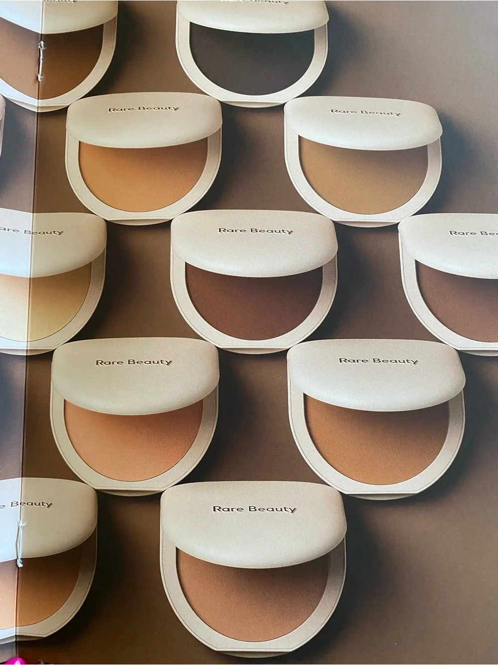 Rare Beauty pressed powder compacts in warm beige and tan tones